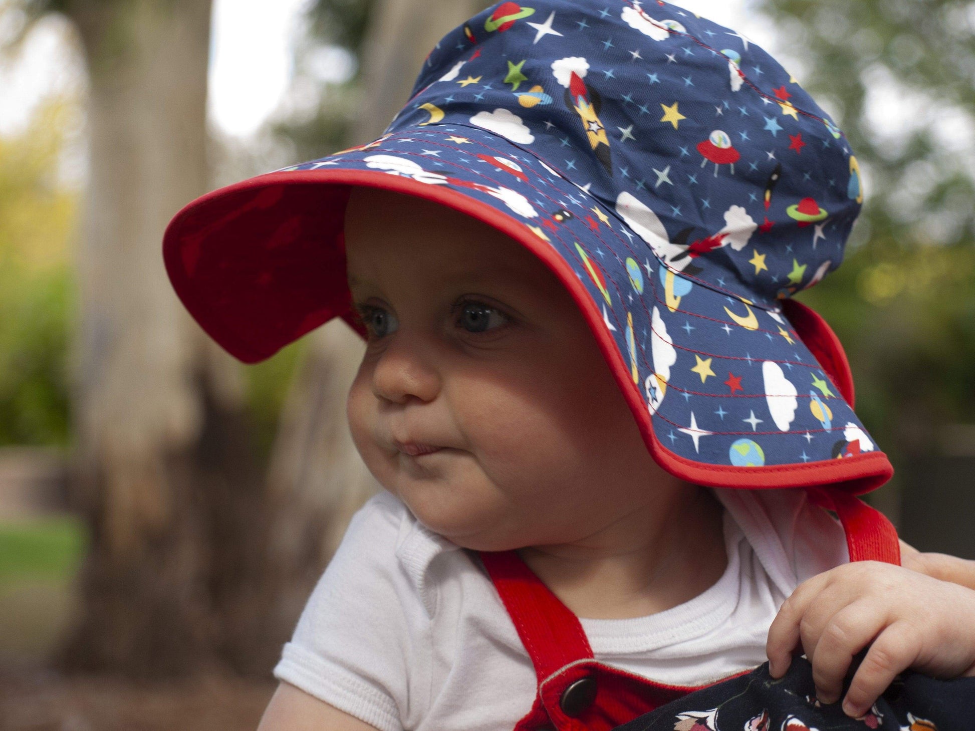 young child wearing overalls and a banz reversible bucket hat outside - background is blurred trees