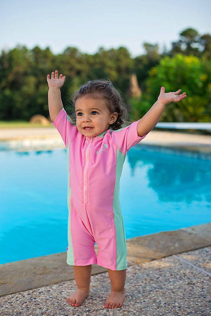 young girl has her hands in the air smiling near a swimming pool wearing a banz one piece swim suit